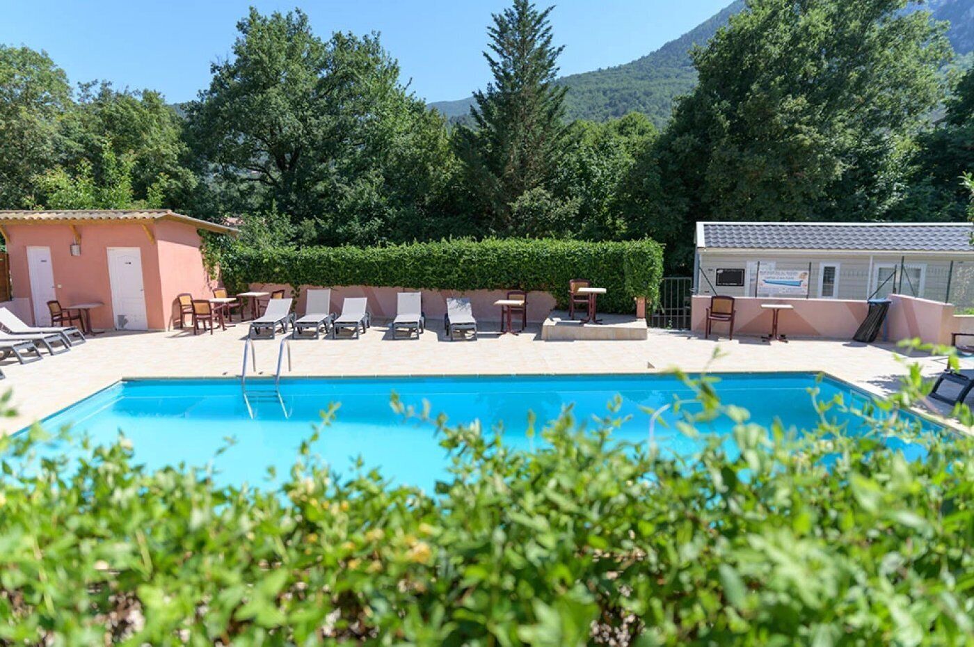 Ein Schwimmbecken mit Liegestühlen und Tischen, umgeben von Grünpflanzen und einem Bergpanorama.