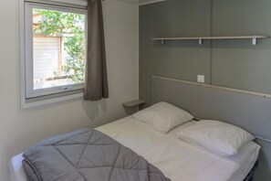 Una cama individual con cabecera, una mesita de noche, una ventana con cortinas y vistas al exterior.