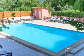 Ein rechteckiger Pool mit Fliesen umgeben, mit Liegestühlen und einem kleinen Gebäude mit Tür und Fenstern.