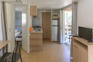 A compact kitchen with a microwave, refrigerator, and a small dining area with a table and chairs. - Camping 2 étoiles - Piscine  - ccbgbhe (Sospel)