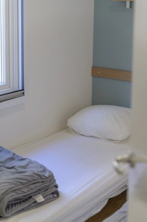 A single bed with a wooden headboard, a window with blinds, and a folded blanket on the bed. - Camping 2 étoiles - Piscine  - ccbgbhe (Sospel)