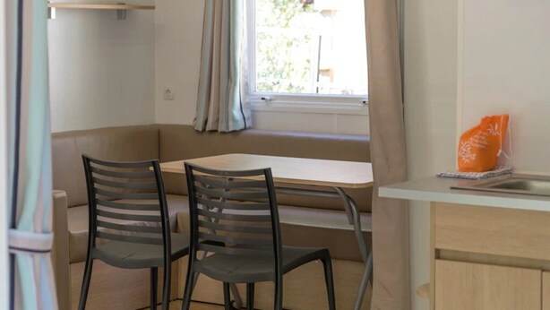 A compact kitchen with a dining table, chairs, a window with curtains, and a small cabinet. - Camping 2 étoiles - Piscine  - ccbgbhe (Sospel)