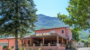 A building with a sign indicating a restaurant, outdoor seating, and a mountain in the background. - Camping 2 étoiles - Piscine  - ccbgbhe (Sospel)