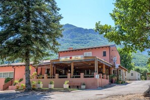 A building with a sign indicating a restaurant, outdoor seating, and a mountain in the background. - Camping 2 étoiles - Piscine  - ccbgbhe (Sospel)