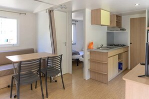 Een knus woongedeelte met een kitchenette, een eethoek met een tafel en stoelen, en een kleine slaapkamer die door een geopende deur zichtbaar is.