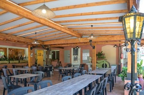 Ein Café im Freien mit Holzbalken, Tischen, Stühlen und hängenden Lampen.