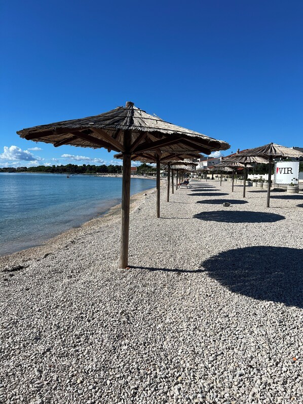A pebbled beach with thatched umbrellas and a clear blue sky. - Apartment with large terrace (Vir)