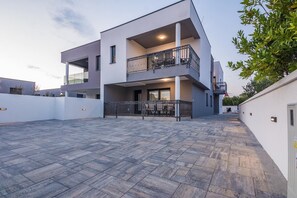 A modern two-story building with a flat roof, a balcony on the upper floor, and a paved courtyard. - Apartment with large terrace (Vir)