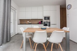 A modern kitchen with white cabinets, a wooden dining table, and white chairs. - Apartment with large terrace (Vir)