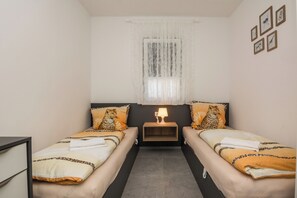 A twin room with two beds, a nightstand with a lamp, a window with sheer curtains, and wall-mounted pictures. - Apartment with large terrace (Vir)