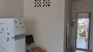 A kitchen with a white refrigerator, a chair, a decorative wall piece, and a door leading to a balcony. - Simplicity and Prime Location in Manaus. (Manaus)
