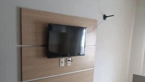 A room with a wall-mounted TV, a bed with a floral bedspread, and a wooden panel wall design. - Simplicity and Prime Location in Manaus. (Manaus)