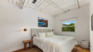 A bedroom with a bed, a nightstand, a window with a view, and a ceiling with exposed beams.