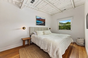 A bedroom with a bed, a nightstand, a window with a view, and a ceiling with exposed beams.