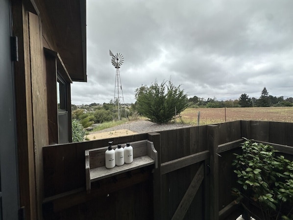 Una estructura de madera con una ventana, un molino de viento metálico y una cerca de madera.