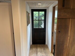 A narrow hallway with a wooden floor, a black door with a window, and a wooden door frame.
