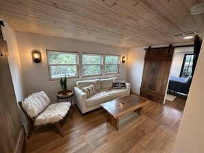 A cozy living room with a wooden ceiling, a white sofa, a wooden bench, and a small side table with a plant.