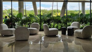 A spacious indoor area with large windows, several comfortable chairs, and a view of lush greenery outside. - MODERN APT WITH SEA VIEW AND SWIMMING POOLS 1 BEDROOM WITH BALCONY. MANZANILLO BEACH. (CARTAGENA)