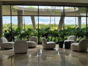 A spacious indoor area with large windows, several comfortable chairs, and a view of lush greenery outside. - MODERN APT WITH SEA VIEW AND SWIMMING POOLS 1 BEDROOM WITH BALCONY. MANZANILLO BEACH. (CARTAGENA)