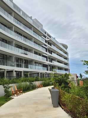 A multi-story hotel with balconies, a concrete pathway, and greenery. - MODERN APARTMENT WITH OCEAN VIEWS AND SWIMMING POOLS; 1 BEDROOM WITH A BALCONY. MANZANILLO BEACH. (CARTAGENA)