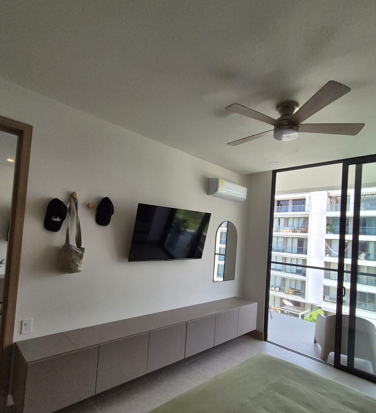 Quarto de hotel moderno com televisão de tela plana, ventilador de teto e grandes janelas com vista para o exterior do edifício.