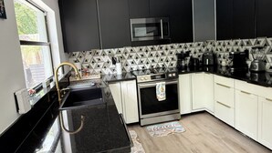 A modern kitchen with black and white cabinetry, a stainless steel microwave, and a coffee maker. - Rabelo’s House
Awesome 5-bedroom house with AC in charming Tampa (Tampa)
