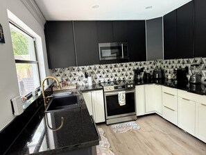 Une cuisine moderne avec des meubles de rangement noirs et blancs, un four à micro-ondes en acier inoxydable et une machine à café.