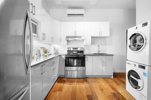 A modern kitchen with stainless steel appliances, white cabinetry, and a wooden floor. - Stylish Loft in the Heart of St-Laurent (Montréal)