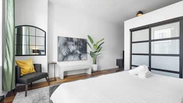 A modern bedroom with a large bed, a bench, a potted plant, and a wall-mounted mirror.