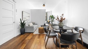 A modern living room with a grey sofa, a dining table with chairs, a coffee table, and a potted plant.