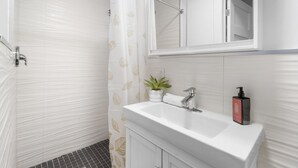 A bathroom with a shower, a sink with a mirror, a potted plant, and a soap dispenser.