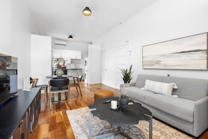 A modern living room with a grey sofa, a coffee table, and a dining area with a table and chairs. - Stylish Loft in the Heart of St-Laurent (Montréal)