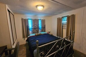 A bedroom with a metal bed frame, a single bed with a blue blanket, a bedside table with a lamp, and a window with curtains.