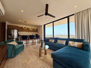 A modern living room with a sofa, chairs, a glass coffee table, and a view of the city through large windows. - Designer 2BR w/ Rooftop Pool, Gym & Stunning Views (Puerto Vallarta)