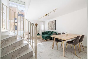 Ein modernes Interieur mit einer Treppe, einem Essbereich, einem grünen Sofa und einem großen Fenster.