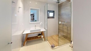A modern bathroom with a glass shower enclosure, a white sink, and a wooden shelf. - Maritime Suites (Hersonissos)