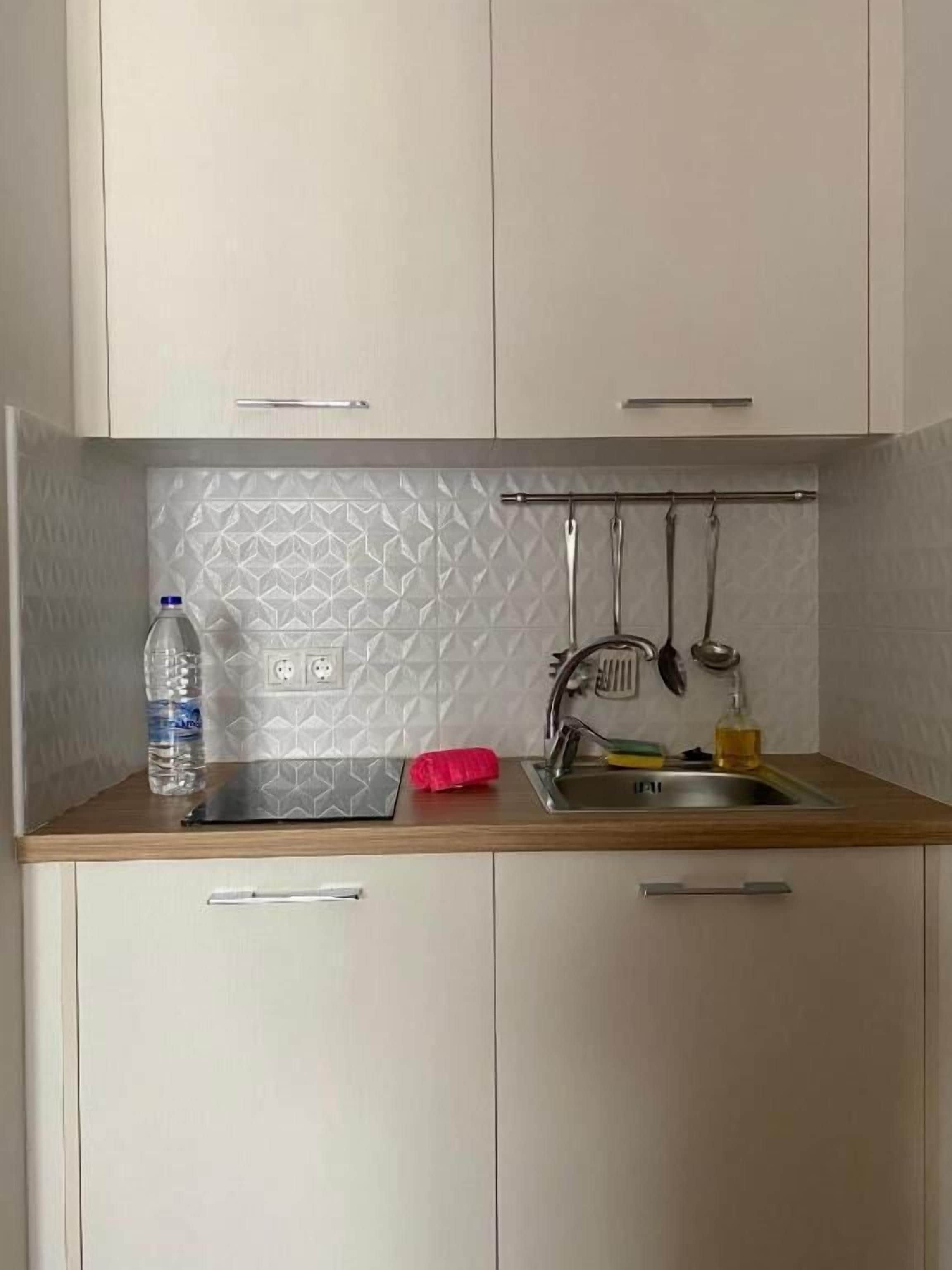 A small kitchenette with a sink, a bottle of water, and a red cloth on the countertop.