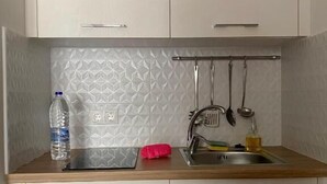 A small kitchenette with a sink, a bottle of water, and a red cloth on the countertop. - Maritime Suites (Hersonissos)