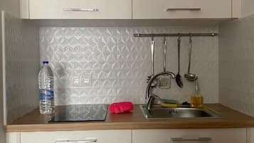 A small kitchenette with a sink, a bottle of water, and a red cloth on the countertop.