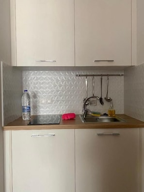 A small kitchenette with a sink, a bottle of water, and a red cloth on the countertop. - Maritime Suites (Hersonissos)
