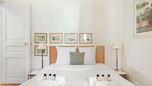 Ein Hotelzimmer mit einem Bett, gerahmten Bildern an der Wand, einer Tür und einem Nachttisch mit einer Lampe.