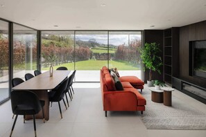 A modern interior with a dining area, sofa, TV, and large windows overlooking a garden. - Woldside - Luxury property sleeps 10 (Bishop Wilton)