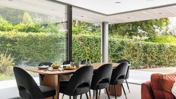 A modern dining area with a wooden table and black chairs, overlooking a lush garden.