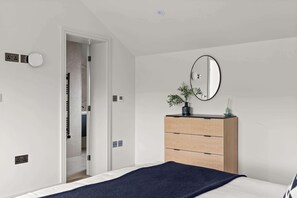 A bedroom with a bed, a dresser, a mirror, and a door leading to a bathroom. - Woldside - Luxury property sleeps 10 (Bishop Wilton)