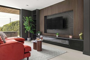 A modern living room with a large flat-screen TV mounted on a wall with a marble-like texture. There is a red sofa, a small round coffee table, and a potted plant.