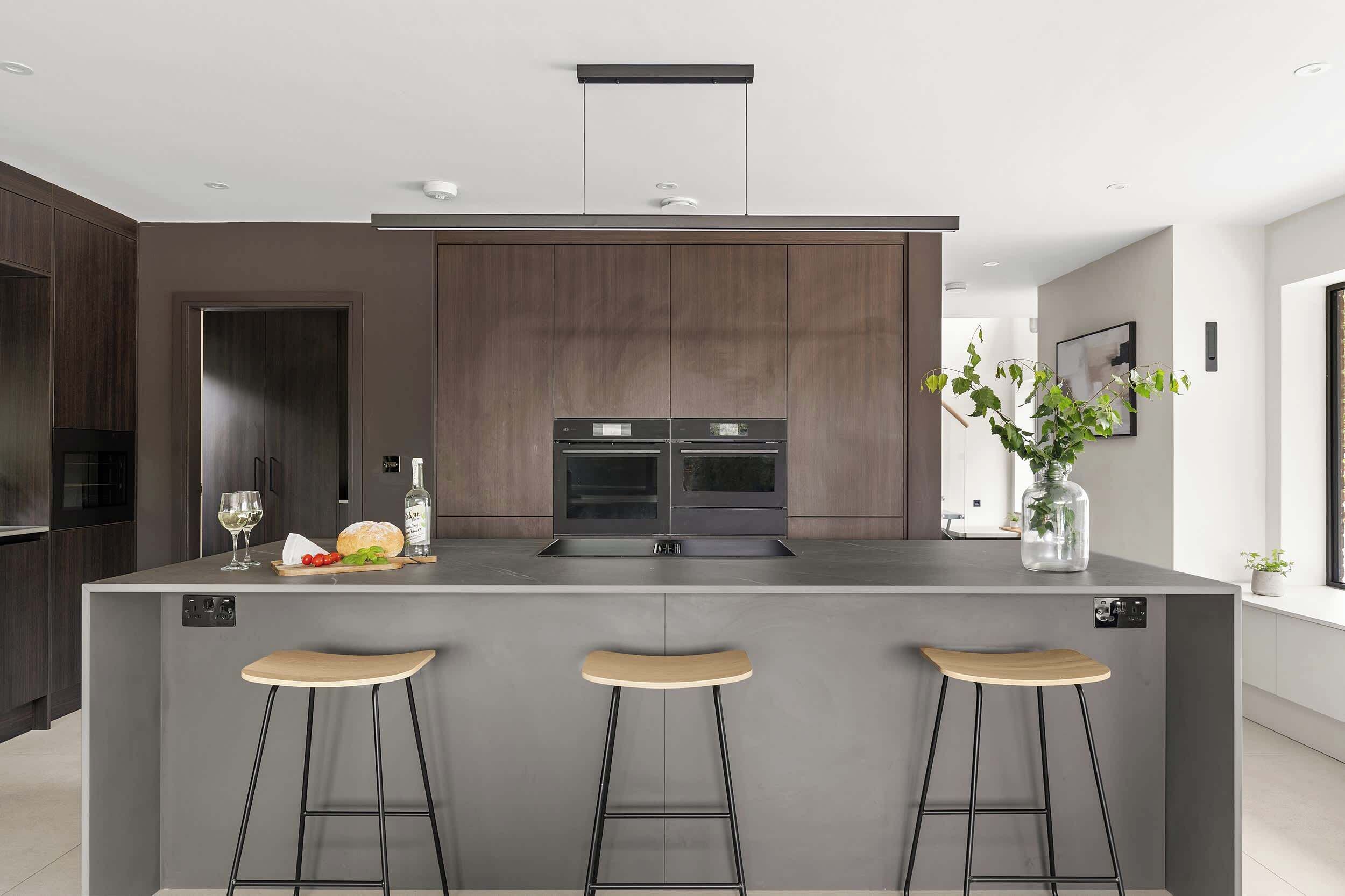 A modern kitchen with a central island, bar stools, and a built-in oven.