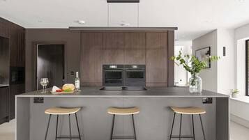 A modern kitchen with a central island, bar stools, and a built-in oven.