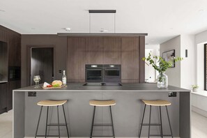 A modern kitchen with a central island, bar stools, and a built-in oven.