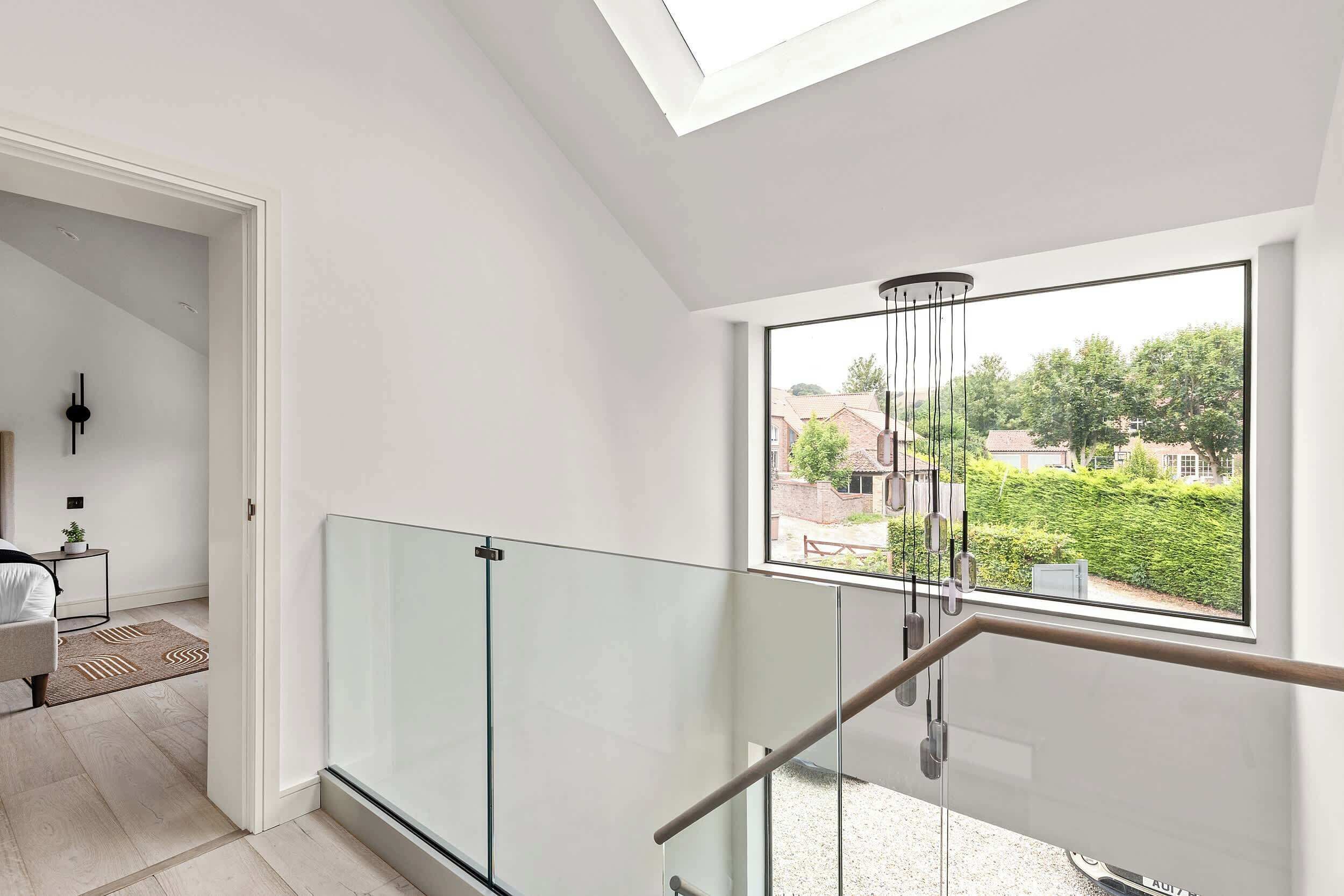 A modern interior with a glass railing, a staircase, and a view of a residential area.