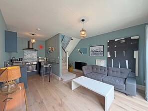 Ein modernes Wohnzimmer mit einem grauen Sofa, einem weißen Couchtisch und einer Küchenzeile mit Herd und Barhocker.